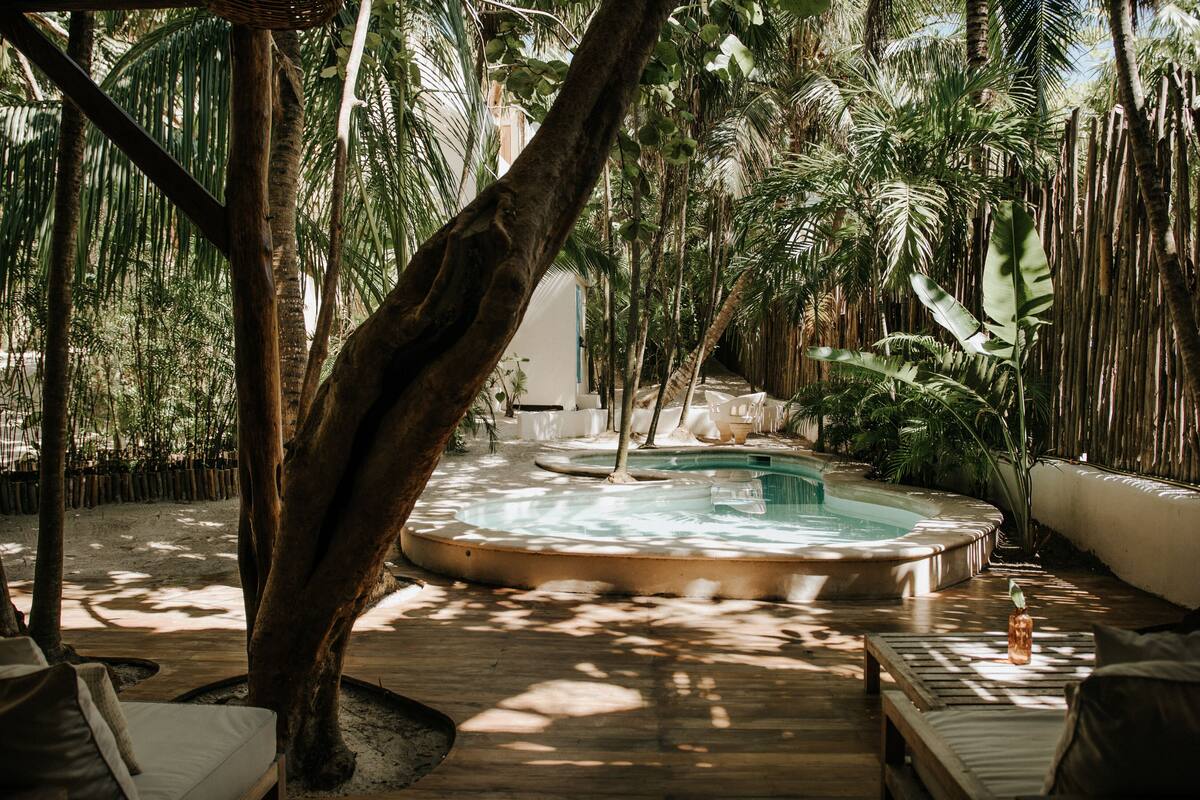 Ein Whirlpool, umgeben von üppiger tropischer Vegetation, einer Holzterrasse und Liegestühlen.