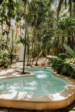 A pool surrounded by lush greenery and palm trees, with a white building in the background. - Mahayana Tulum Beach Homes (Tulum)