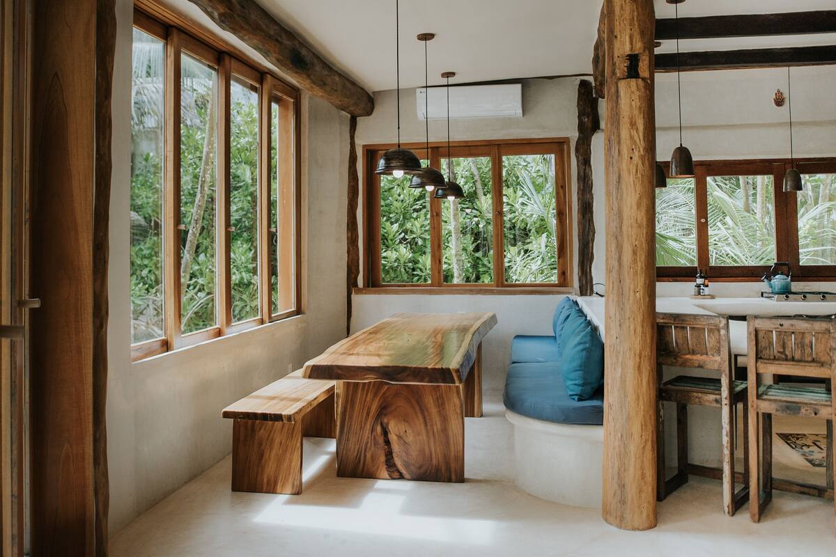 Ein rustikales Holzinterieur mit großen Fenstern, einer hölzernen Bank, einem blau gepolsterten Sitz und einem Holztisch.