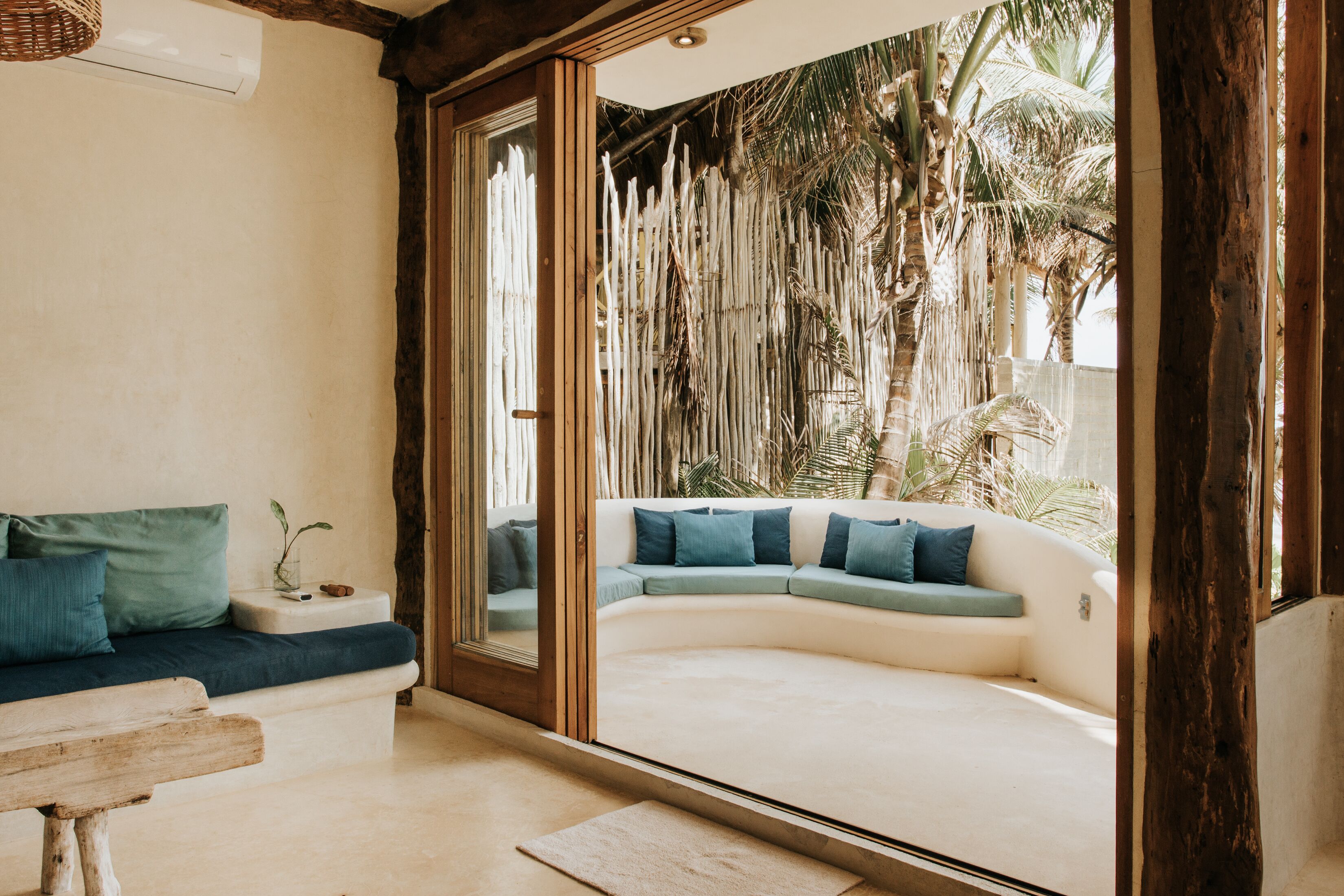 A modern living room with a curved sofa, a wooden bench, and a large window overlooking a tropical garden.