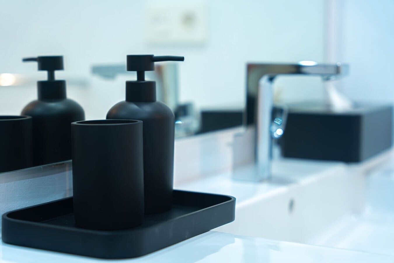 Un baño moderno con un dispensador de jabón negro y un grifo cromado sobre una encimera blanca.