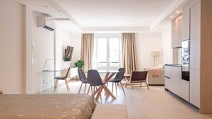 Une chambre d’hôtel moderne équipée d’un lit, d’un bureau, de chaises, d’un canapé, d’une kitchenette et d’une grande fenêtre.