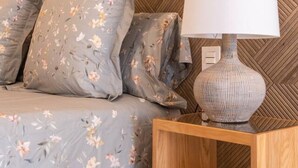 A bed with floral bedding, a wooden nightstand with a lamp, and a herringbone-patterned wall. - Rooms & Suites Loft 2F en el Centro de Arrecife (Arrecife)