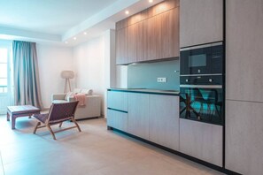Une cuisine moderne dotée d’appareils électroménagers intégrés, un coin repas avec une chaise et une table, et une grande fenêtre avec des rideaux.