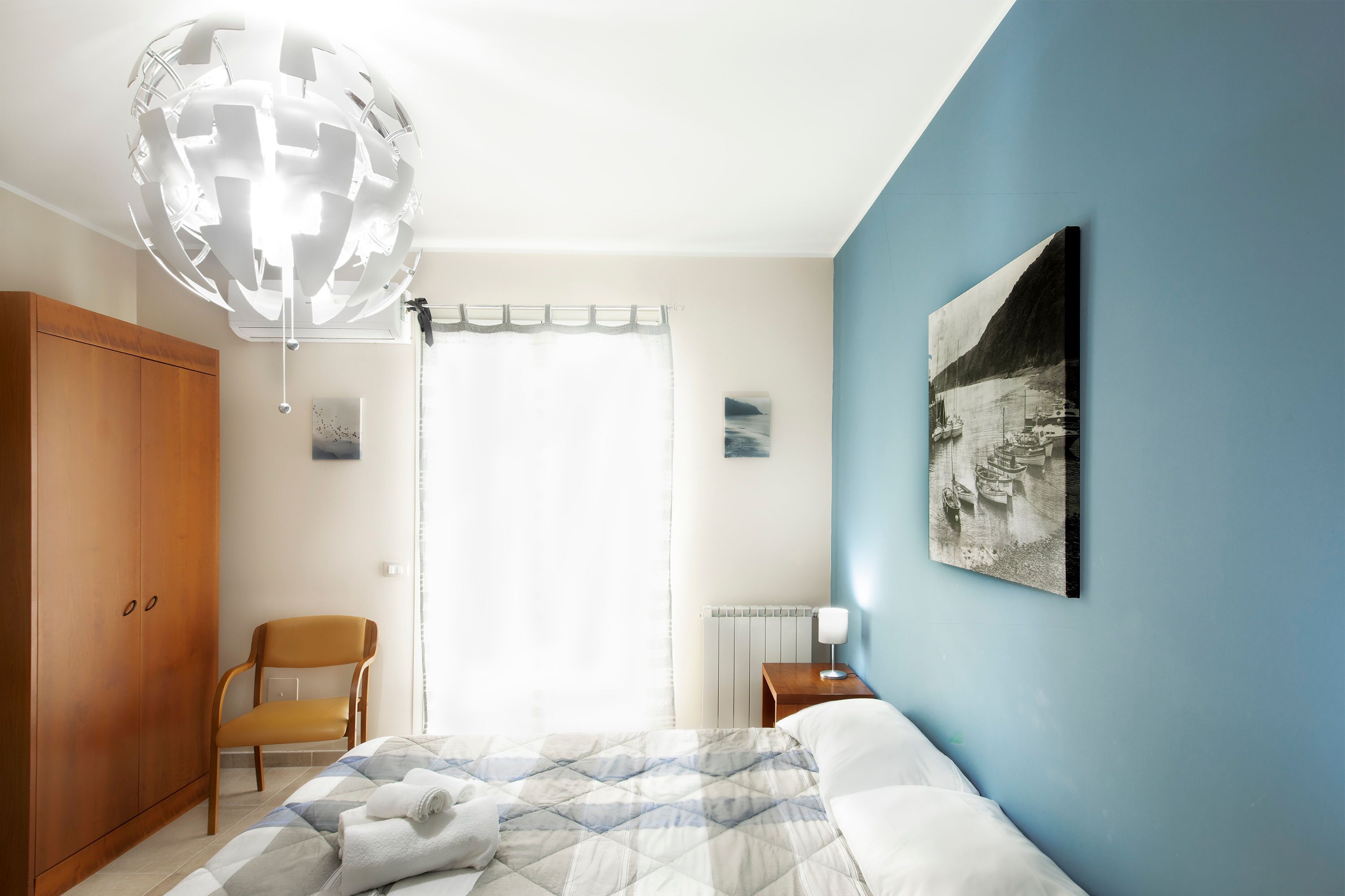 Un dormitorio con cama, una silla, un armario, un radiador y un cuadro en la pared.