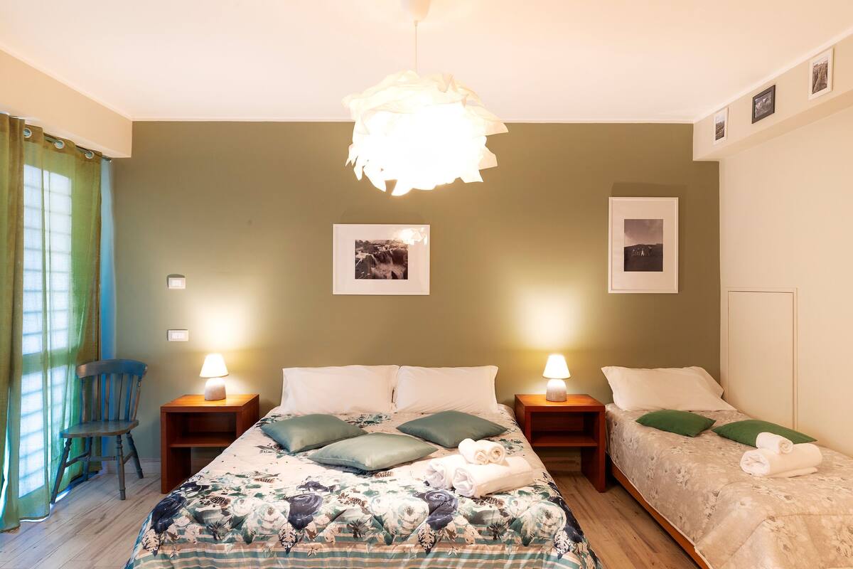Un dormitorio con dos camas, una silla y una mesita de noche con lámpara.