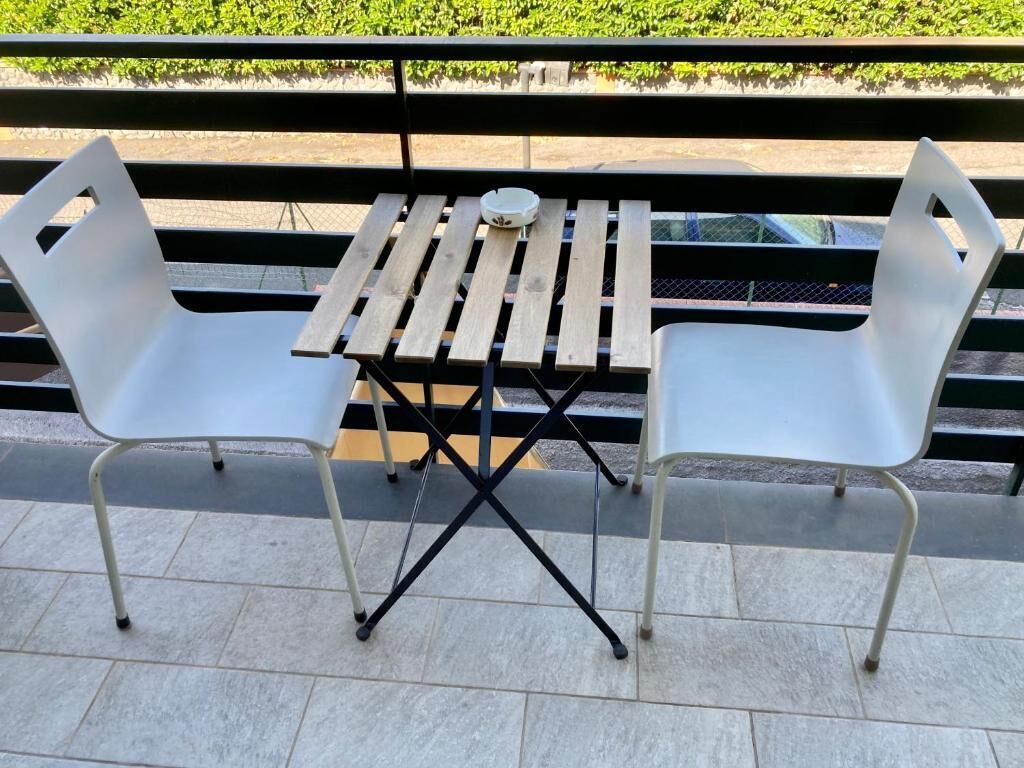 A patio with a wooden table and two white chairs.