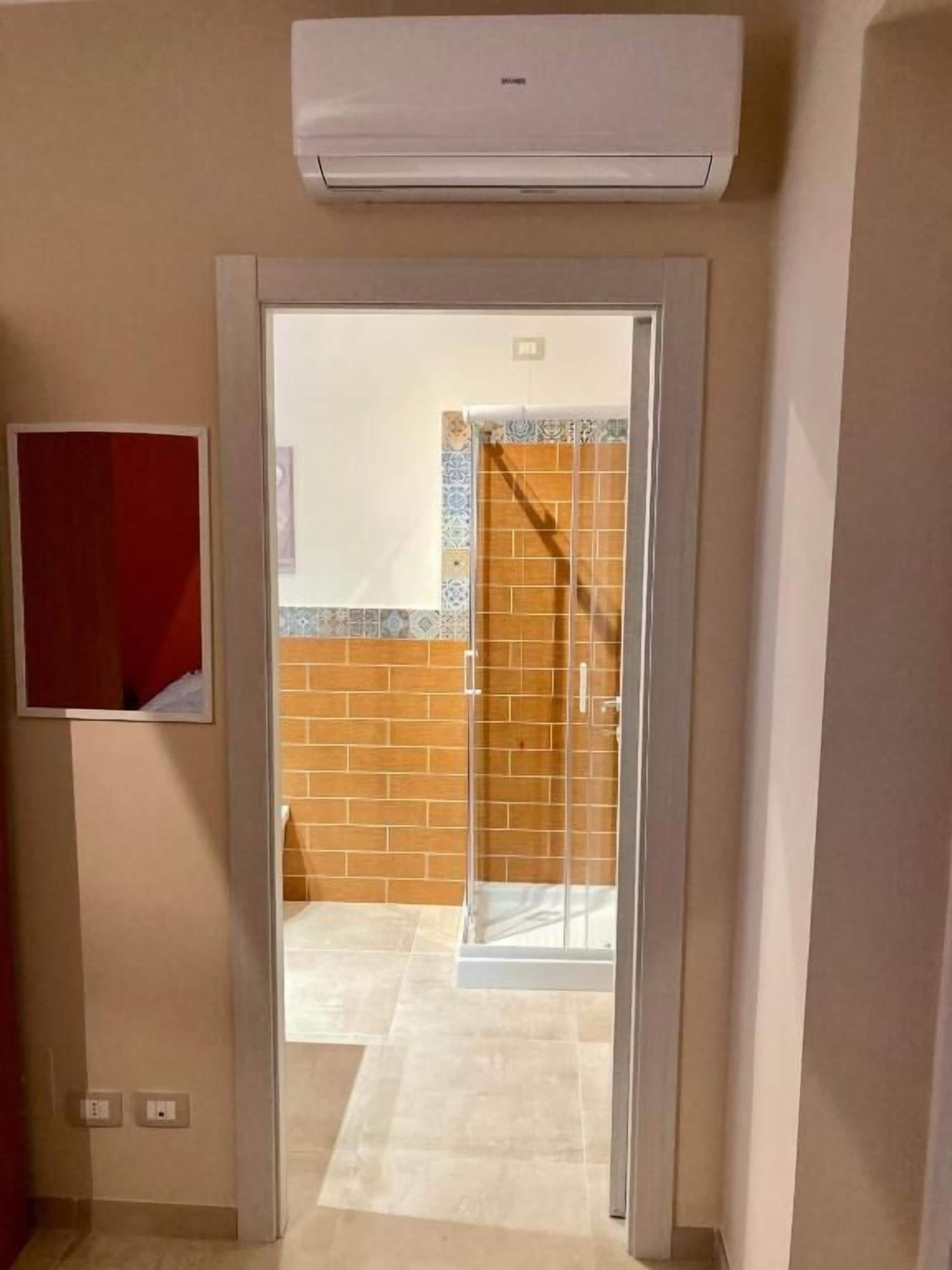 A hotel room entrance with a sliding glass door, a red-framed mirror, and a tiled floor.