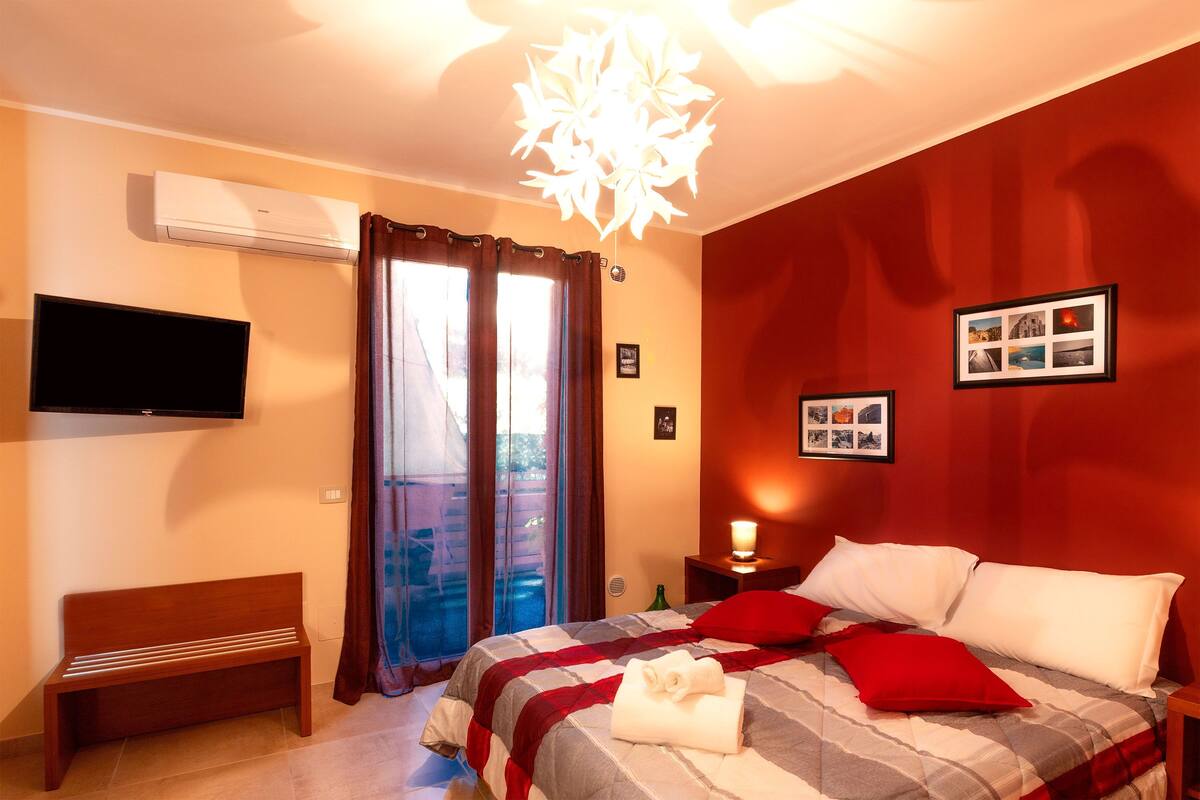 Un dormitorio con cama, un banco, un televisor y una ventana con cortinas.