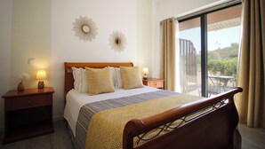 Een hotelkamer met een groot bed, twee nachtkastjes met lampen, een raam met gordijnen en decoratieve wandlampen.