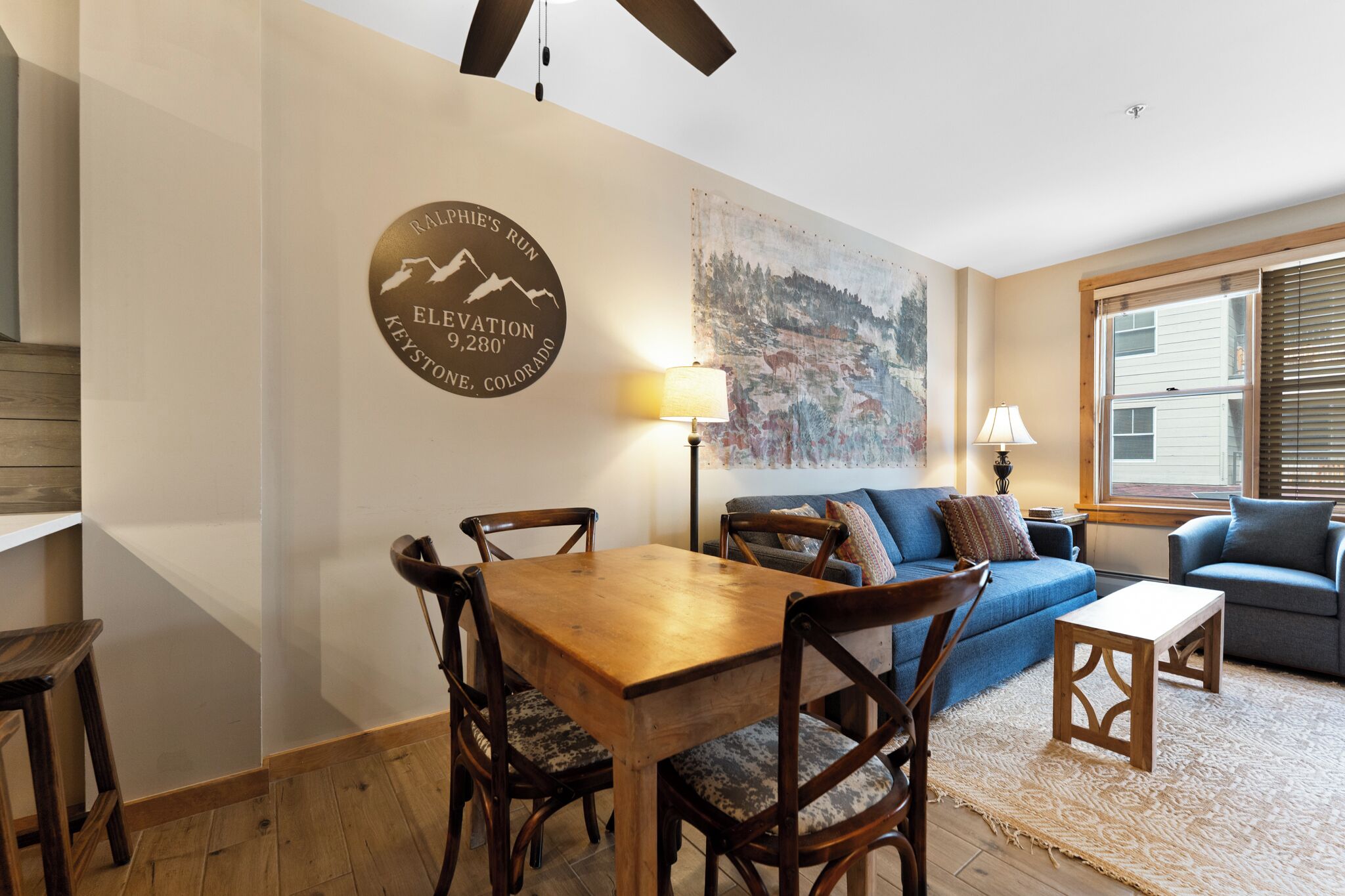 Un comedor con mesa y sillas de madera, un sofá, una lámpara y un letrero en la pared.