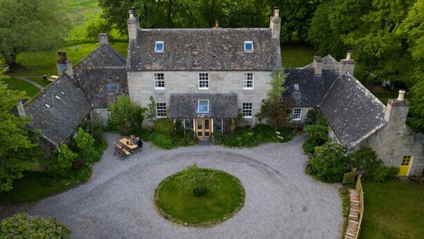 A large stone building with a symmetrical facade, multiple chimneys, and a central entrance. - Dell Cottage (Nethy Bridge)