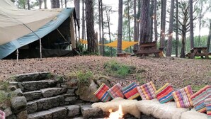 A stone fire pit with a fire burning, surrounded by colorful cushions and a tent in a forested area. - South Dell - Scandi-style family cottage set on the edge of the Abernethy Forest (Nethy Bridge,)