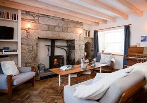 A cozy living room with a stone fireplace, wooden beams, a piano, and comfortable seating. - South Dell (Nethy Bridge,)