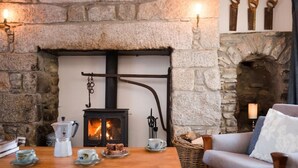 A cozy room with a stone fireplace, a wooden table with plates and cups, and a comfortable chair. - South Dell - Scandi-style family cottage set on the edge of the Abernethy Forest (Nethy Bridge,)
