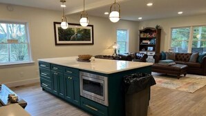A modern kitchen with a central island, wooden flooring, and a dining area with a table and chairs. - Old Southern - Lakefront - Dog friendly (New Tazewell)