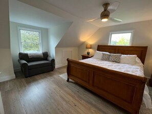 A bedroom with a wooden bed, a dark sofa, and a ceiling fan.