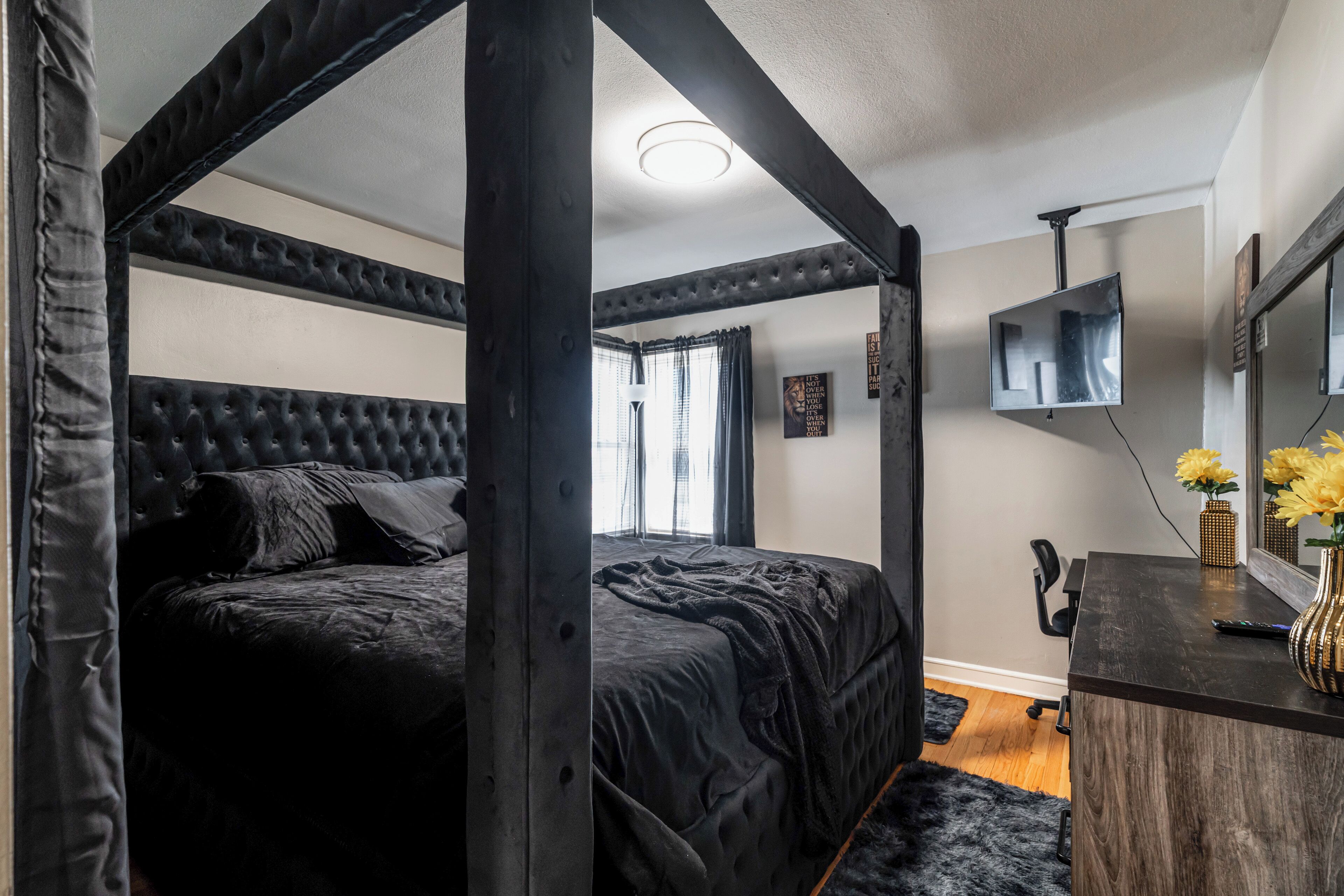 Een slaapkamer met een hemelbed, een bureau met spiegel en een televisie.