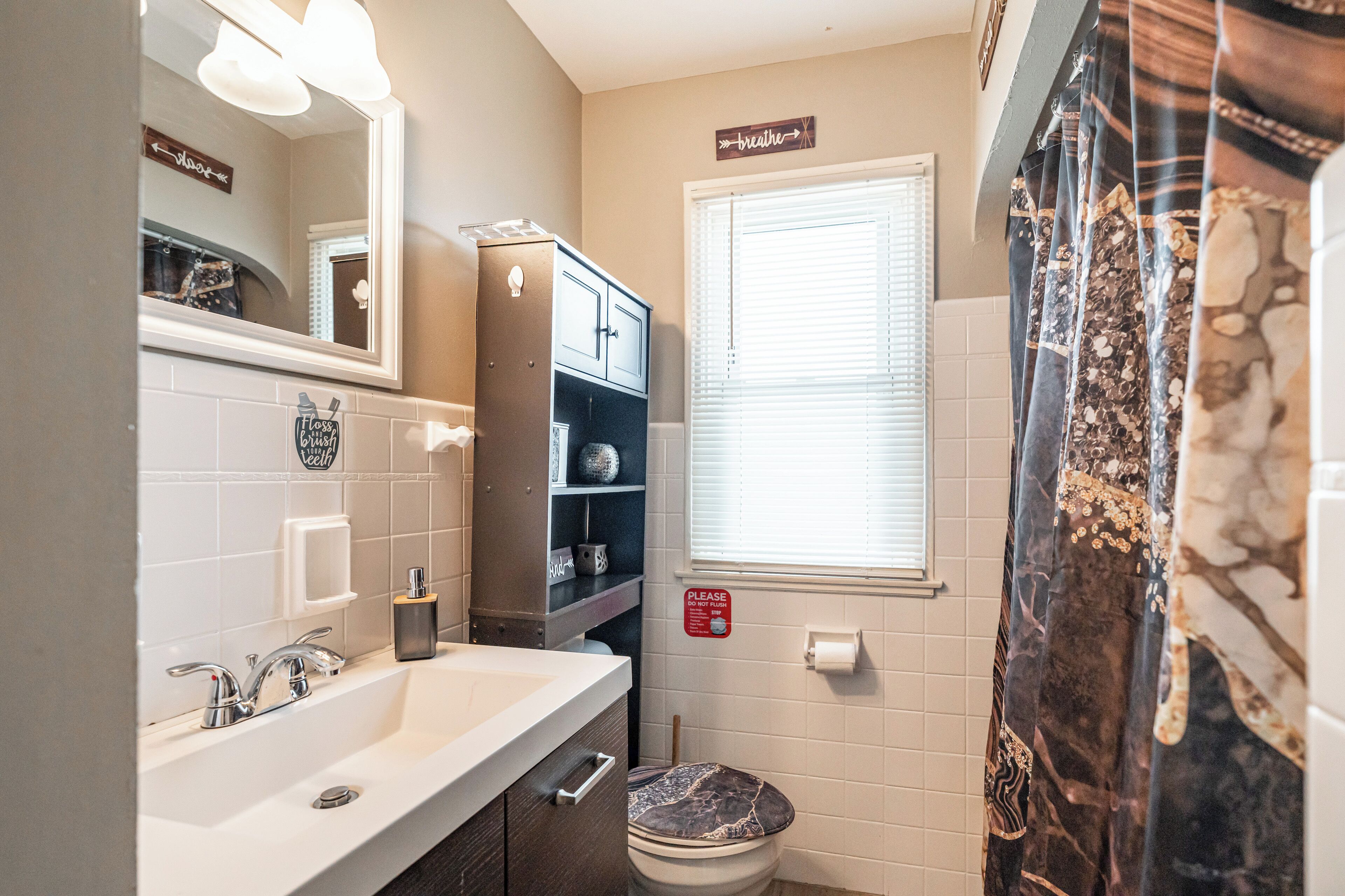 A bathroom with a sink, mirror, toilet, and a window with blinds.