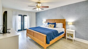 A bedroom with a wooden bed, a ceiling fan, a nightstand with a lamp, and a view of the outside through a door. - New Smyrna Beach Vacation Rental < 1/2 Mi to Beach (New Smyrna Beach)