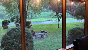 A room with a large window overlooking a grassy area with trees and a bench. - Mountain Lake House - Hot tub, fire pit, fish and swim! (Almond)