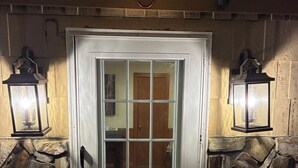 A white door with a glass panel, flanked by two lantern-style lights, set against a stone wall. - Mountain Lake House - Hot tub, fire pit, fish and swim! (Almond)