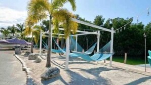 A hammock under a white pergola, surrounded by palm trees and a sandy area. - Key Largo 2 bedroom/1 bath with community pool (Key Largo)