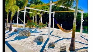 A hammock suspended between white poles in a sandy area with rocks and palm trees. - Key Largo 2 bedroom/1 bath with community pool (Key Largo)
