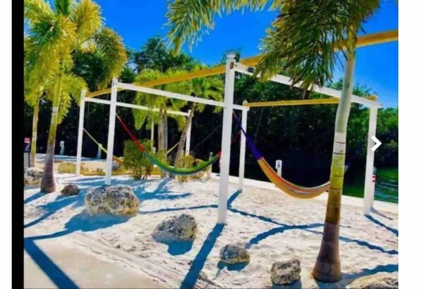 A hammock suspended between white poles in a sandy area with rocks and palm trees. - Key Largo 2 bedroom/1 bath with community pool (Key Largo)