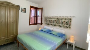 Une chambre à coucher avec un lit, une armoire en bois, une table de chevet, une lampe et une tapisserie au mur.