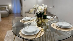 A modern dining area with a glass table set for four, featuring gold and white dinnerware, gold cutlery, and a bottle of champagne. - Bellagio Luxury Suites Apartments (Bellagio)