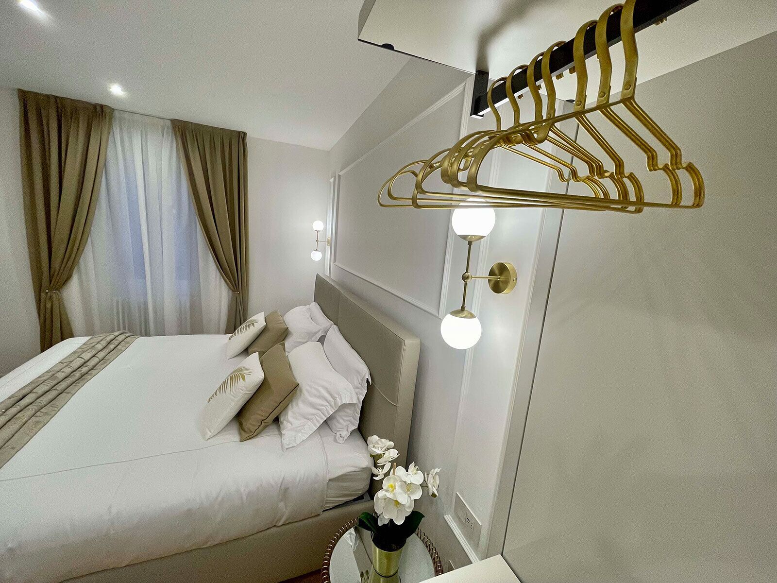 A modern hotel room with a neatly made bed, a wall-mounted light fixture, and a clothing rack.