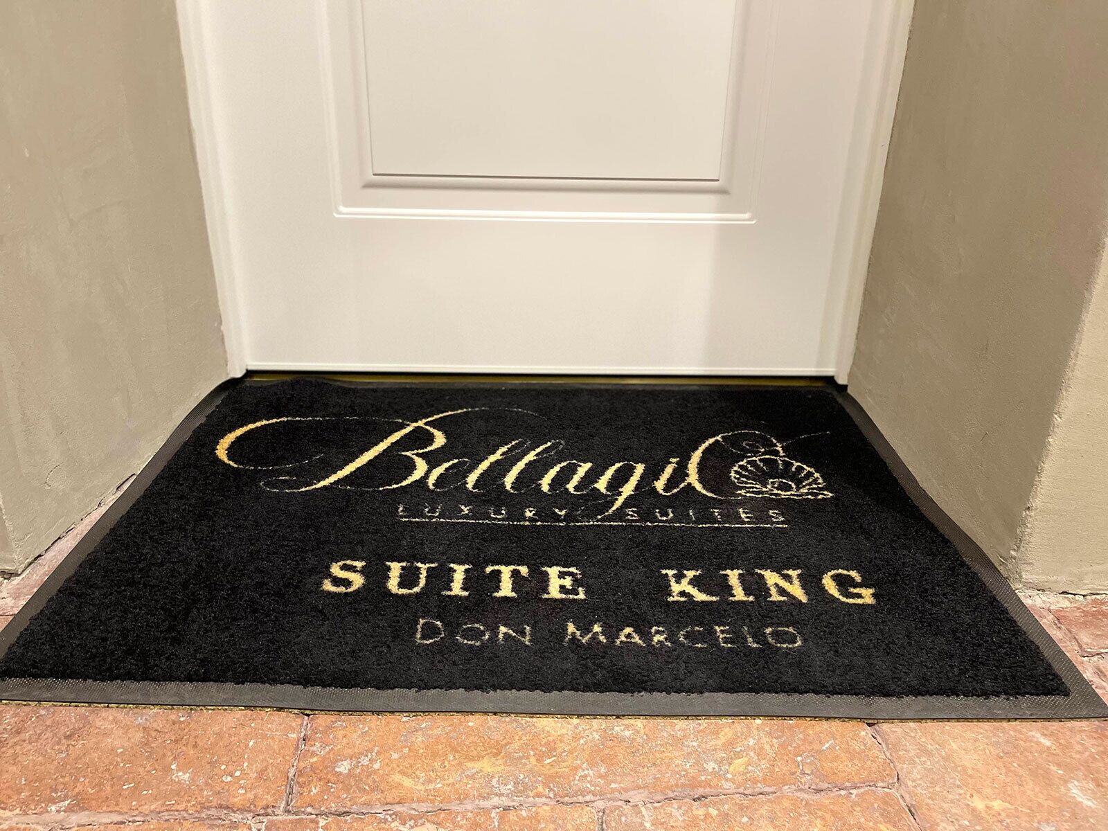 Un felpudo negro con el texto grabado en letras doradas: "Bettagi Luxury Suites" y "Suite King Don Marcelo".