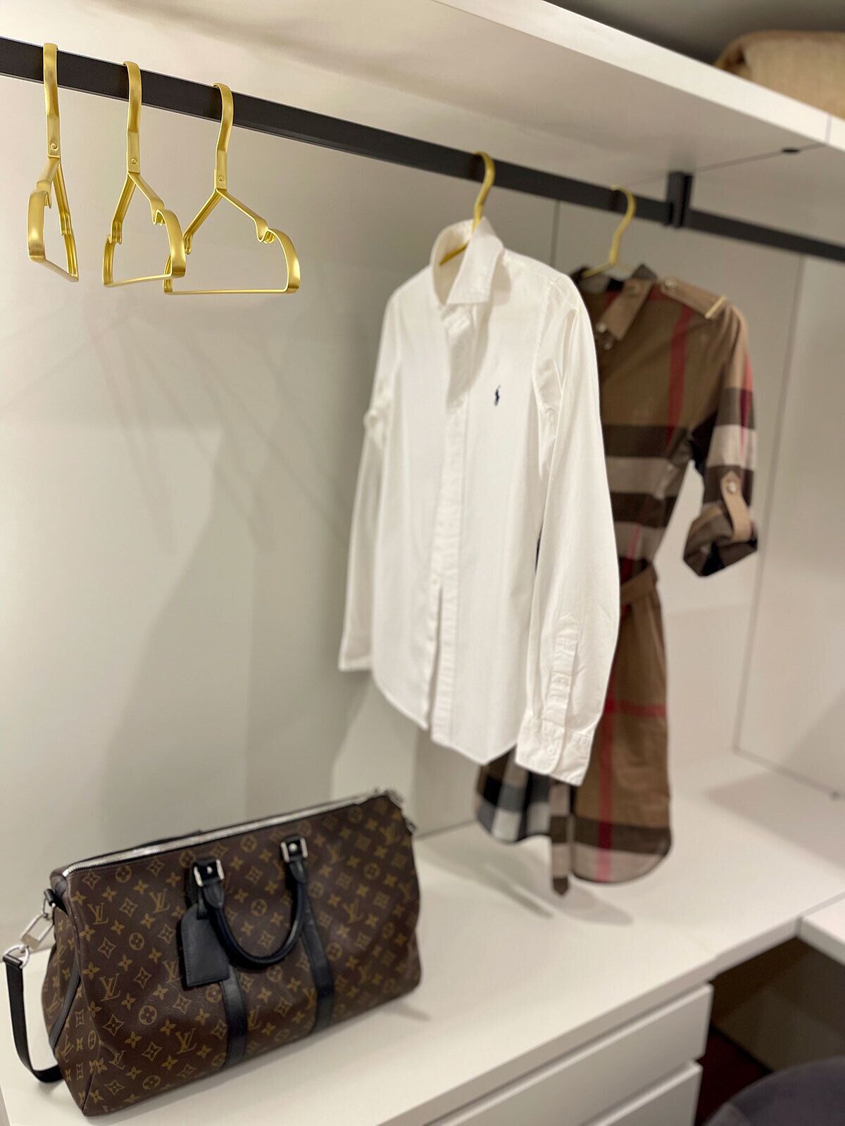 Kledingpresentatie met een wit overhemd, een geruite jurk en een Louis Vuitton tas op een witte plank.