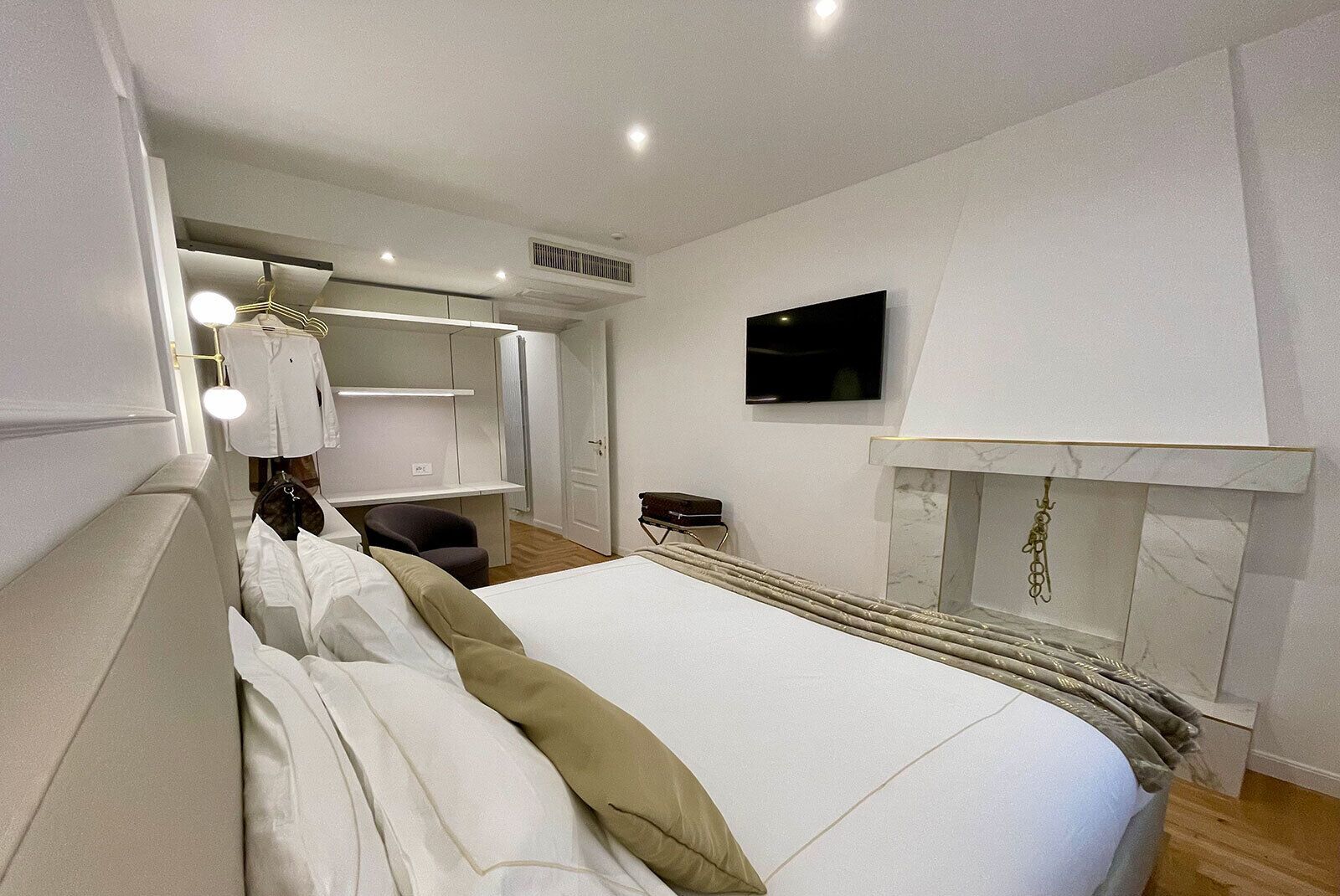 A hotel room with a bed, a TV mounted on the wall, a wardrobe, and a desk with a chair.