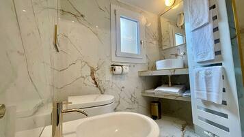 A modern bathroom with a marble wall, a white sink, a gold faucet, a toilet, and a towel rack.