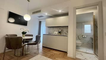 A modern kitchen with white cabinets, a marble countertop, and a built-in oven. There is a dining area with a table and chairs, and a large window providing natural light.