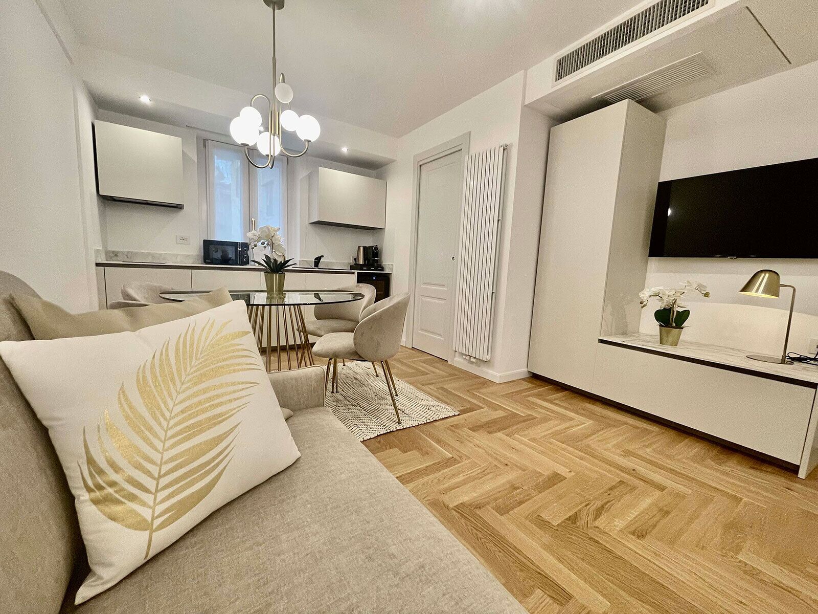 Una sala moderna con un sofá, una mesa de comedor y sillas. Hay una zona de cocina con un microondas y un televisor montado en la pared.