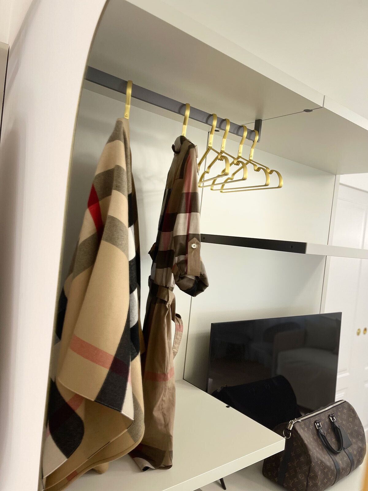 Una habitación con un armario blanco, un televisor de pantalla plana y un bolso Louis Vuitton en el suelo.