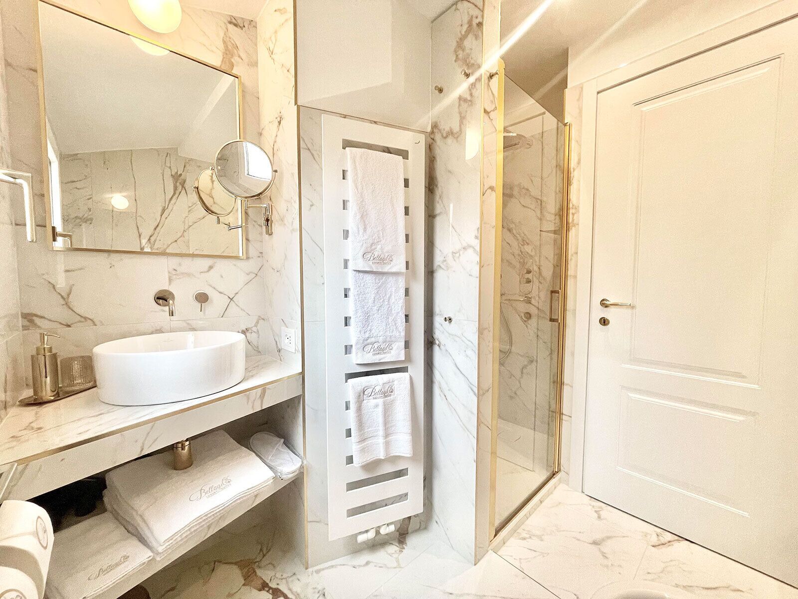 A modern bathroom with a marble sink, a large mirror, a glass-enclosed shower, and a white door.