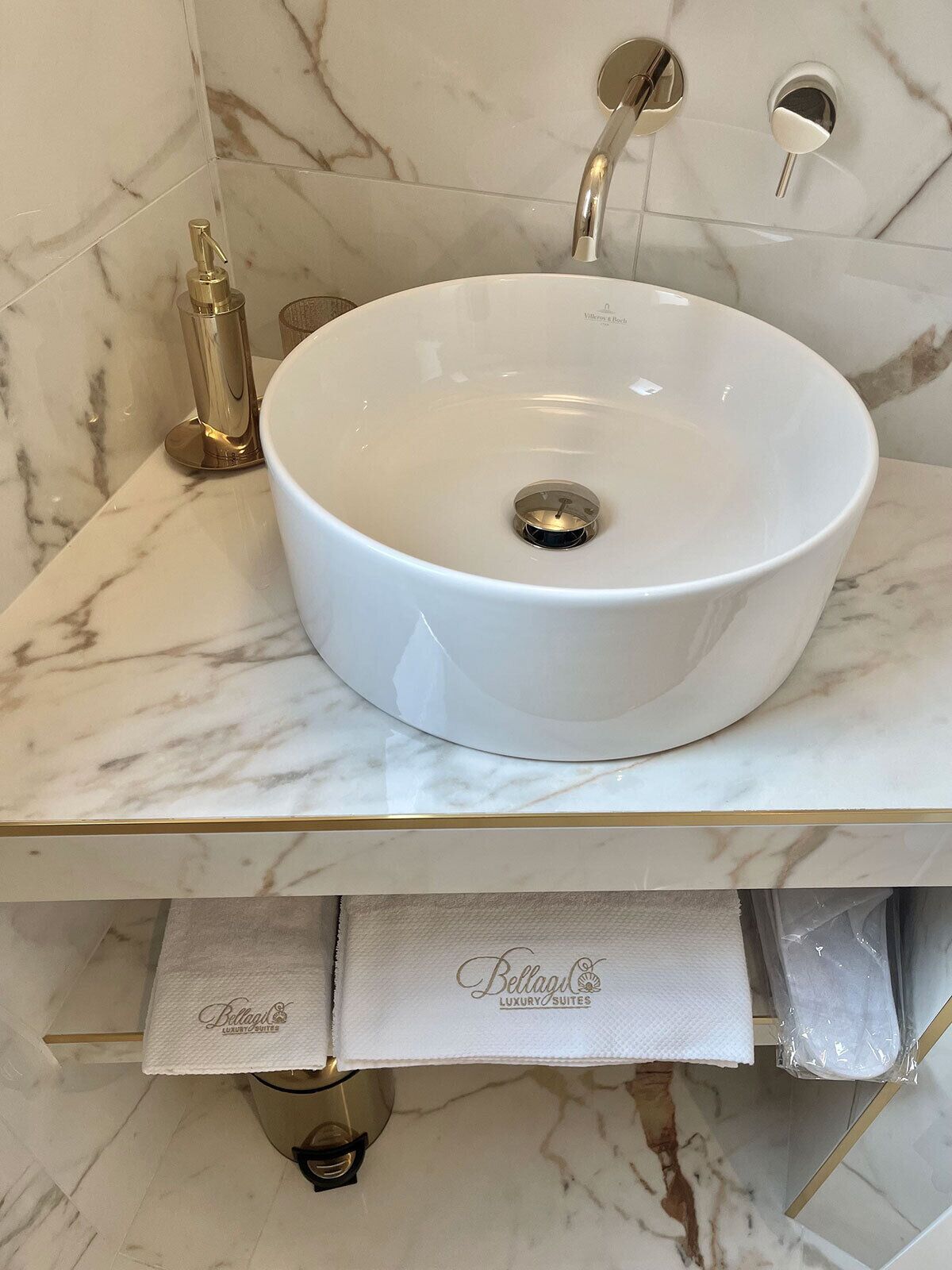 A bathroom with a white marble sink, gold fixtures, and a towel rack labeled "Bellagio Luxury Suites".