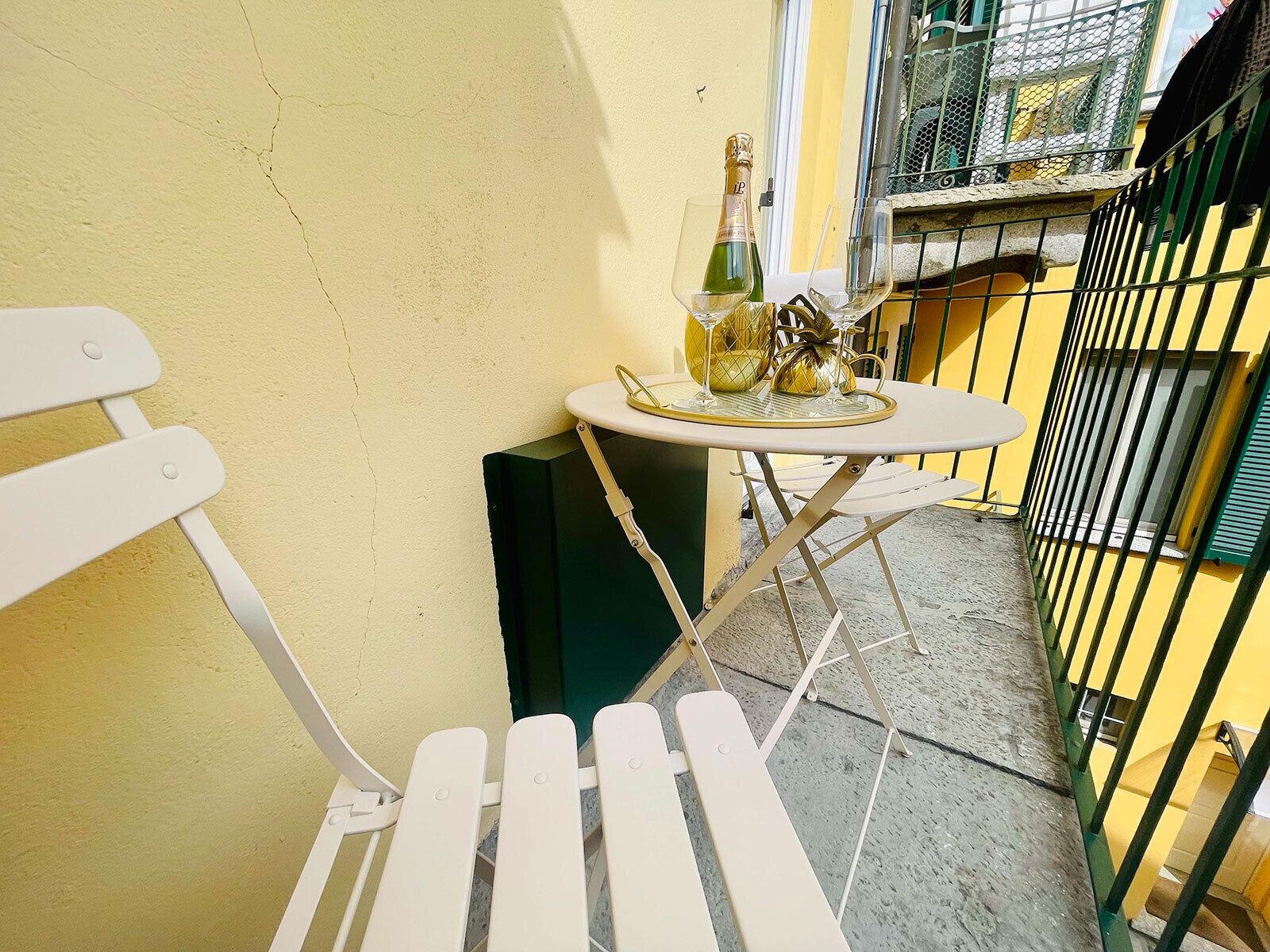 A small outdoor seating area with a white metal chair and a table, a bottle of champagne, and a decorative item on the table.
