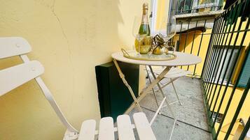 Ein kleiner Außenbereich mit einem weißen Metallstuhl und einem Tisch, einer Champagnerflasche und einem dekorativen Gegenstand auf dem Tisch.