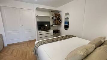 Un dormitorio con cama, armario, espejo y televisión.