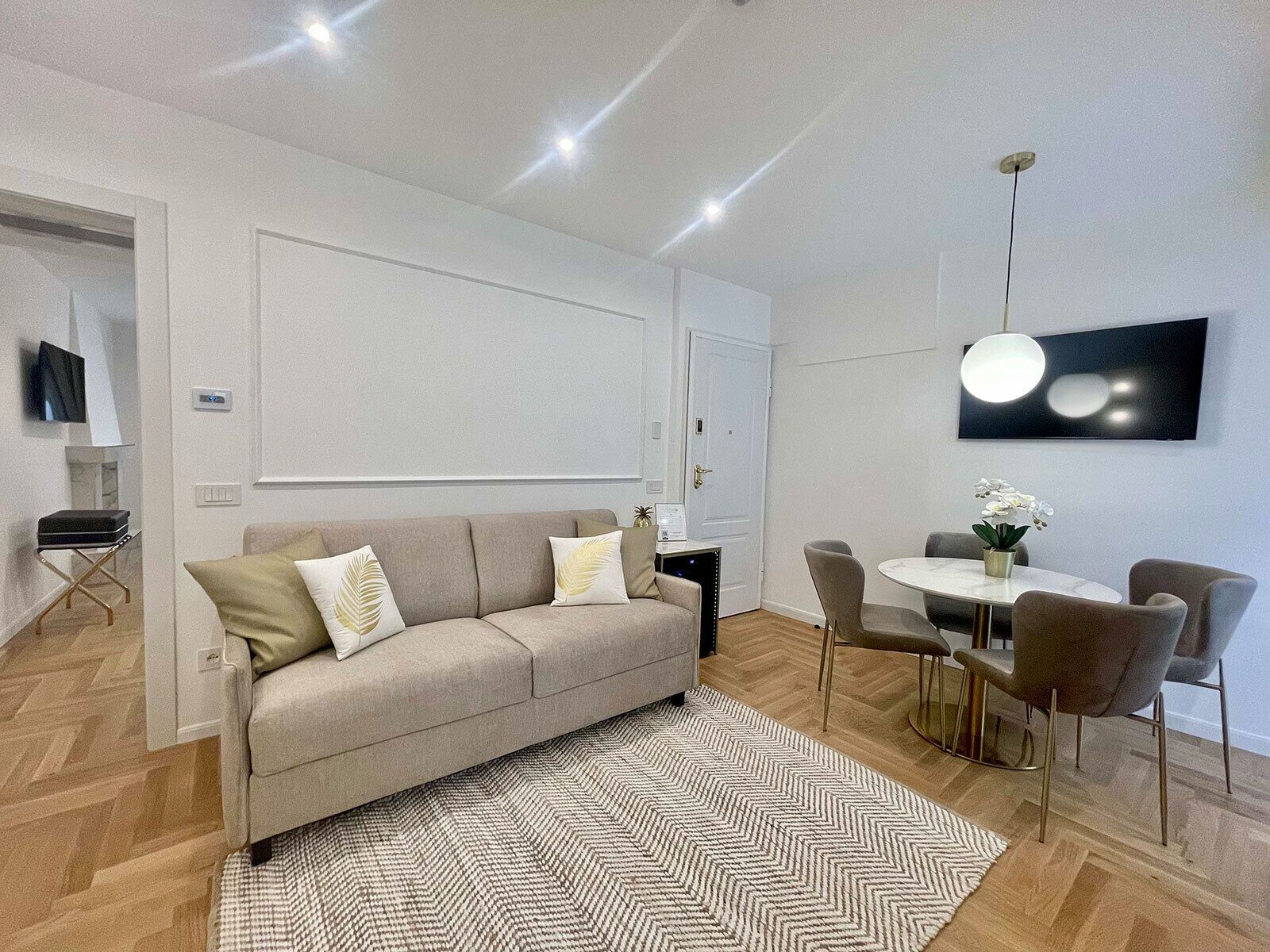 A modern living room with a sofa, a dining table with chairs, and a TV mounted on the wall.