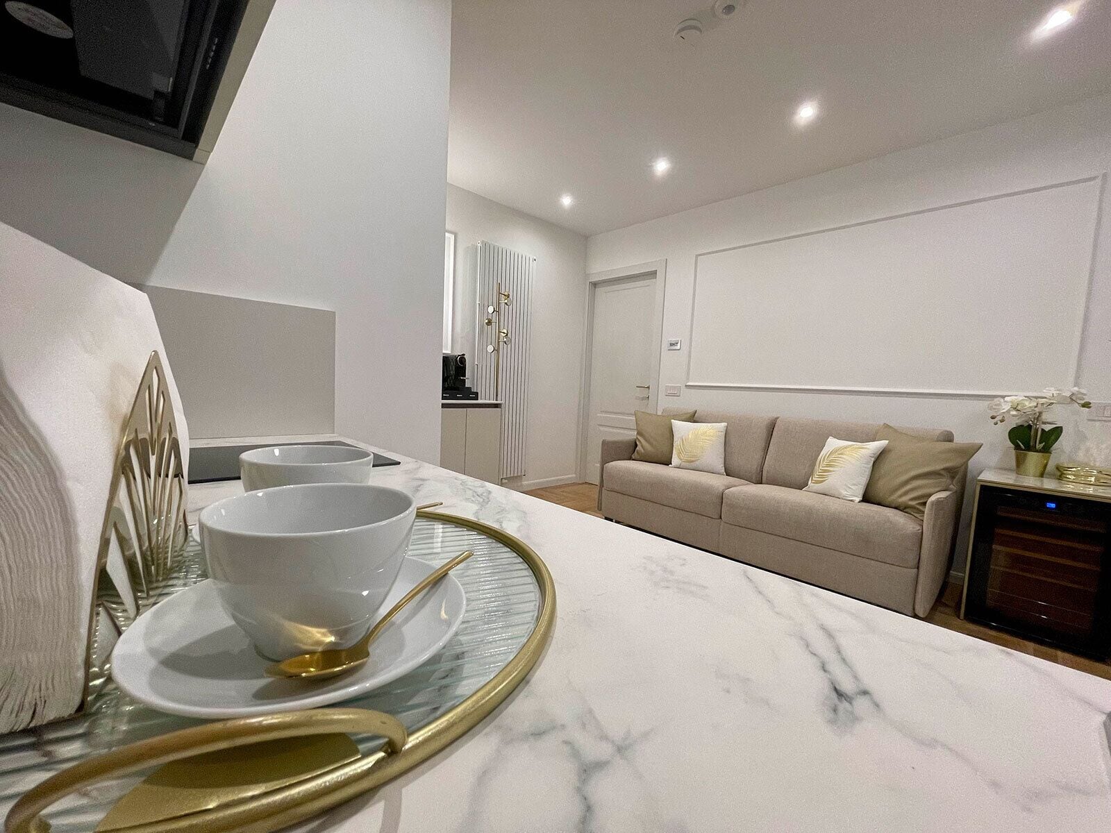 A modern living room with a marble countertop, a sofa, and a dining area with a glass table and gold-rimmed plates.