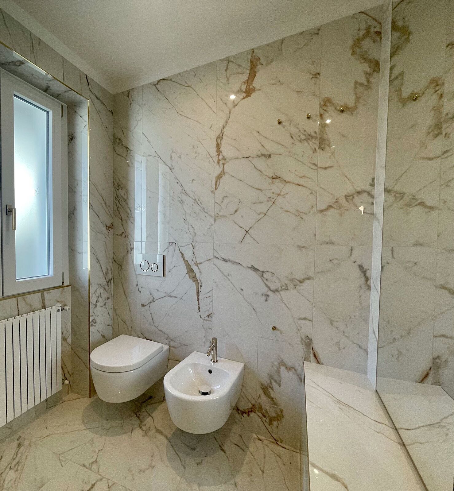 Une salle de bain avec un mur en marbre, un bidet, des toilettes et un miroir.