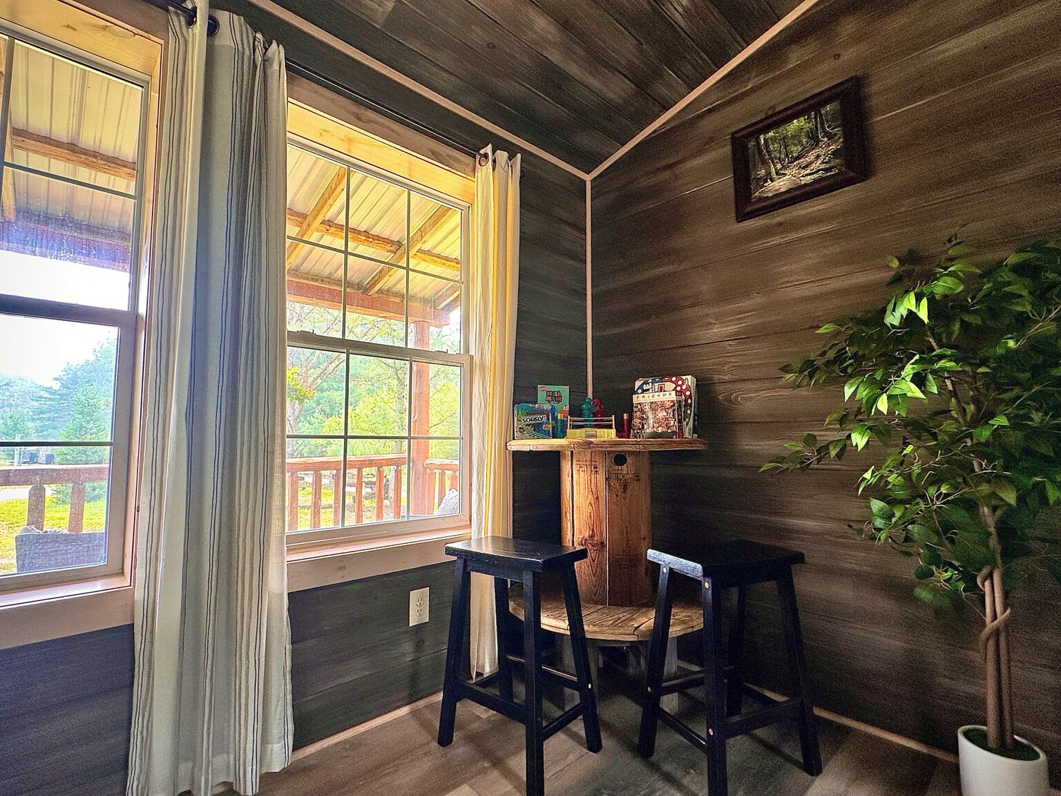 A room with a large window, wooden walls, a small table with chairs, and a potted plant.