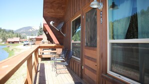 Una baita di legno con una veranda, posti a sedere all'aperto e vista su un lago e le montagne.