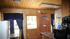 Cucina compatta con mobili in legno, un forno a microonde, una macchina da caffè e una porta con finestra.